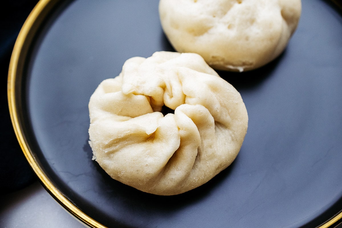 Two Chinese steamed pork dumplings on a dark round plate.