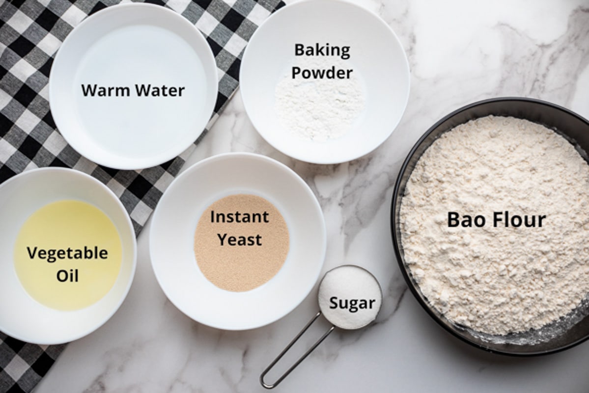 Various bowls filled with ingredients for making pork buns dough, on top of a marble surface.