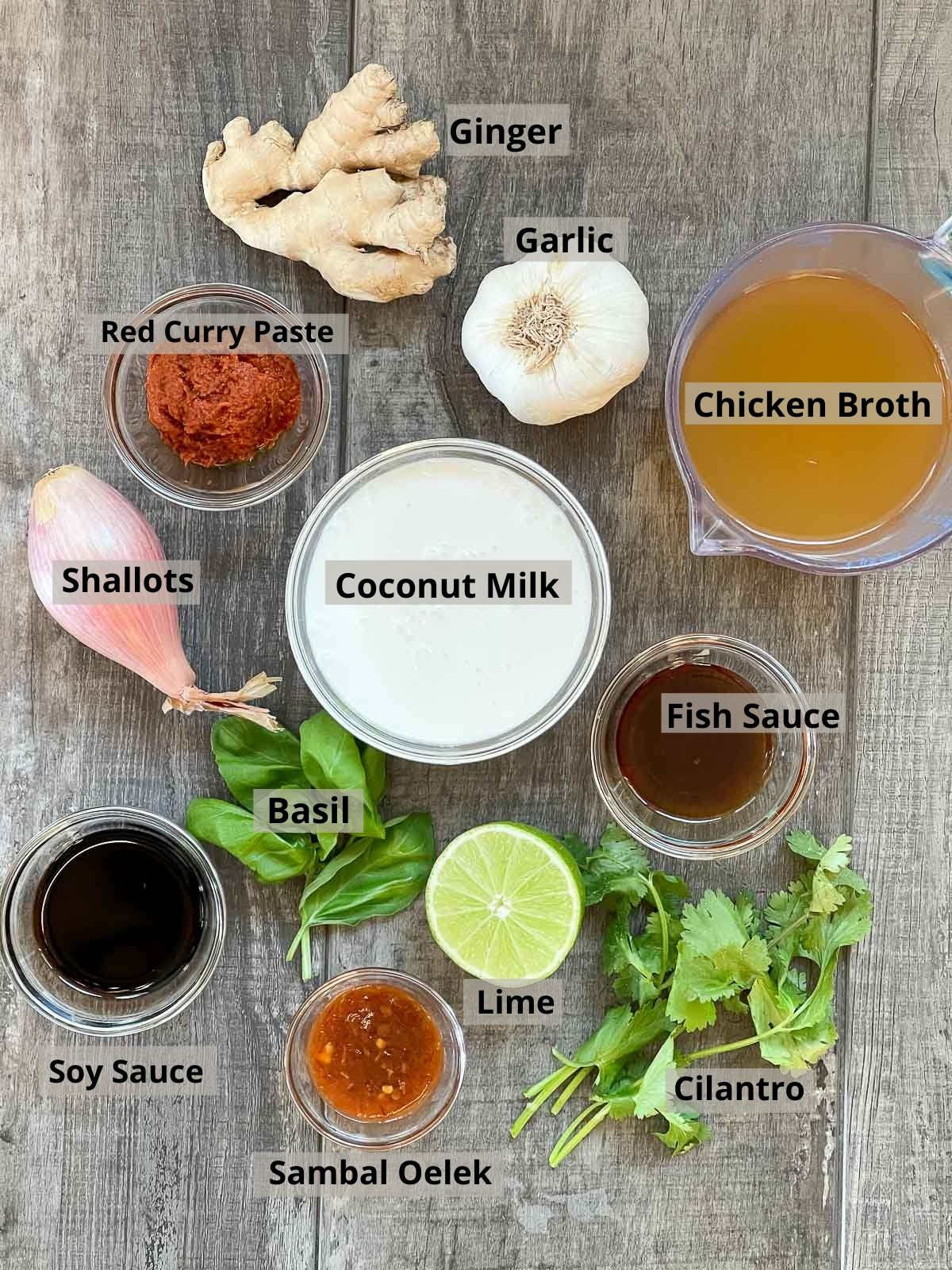 Various glass bowls filled with ingredients for making Thai Coconut Curry Seafood Soup placed on top of a wooden plank board with fresh produce.