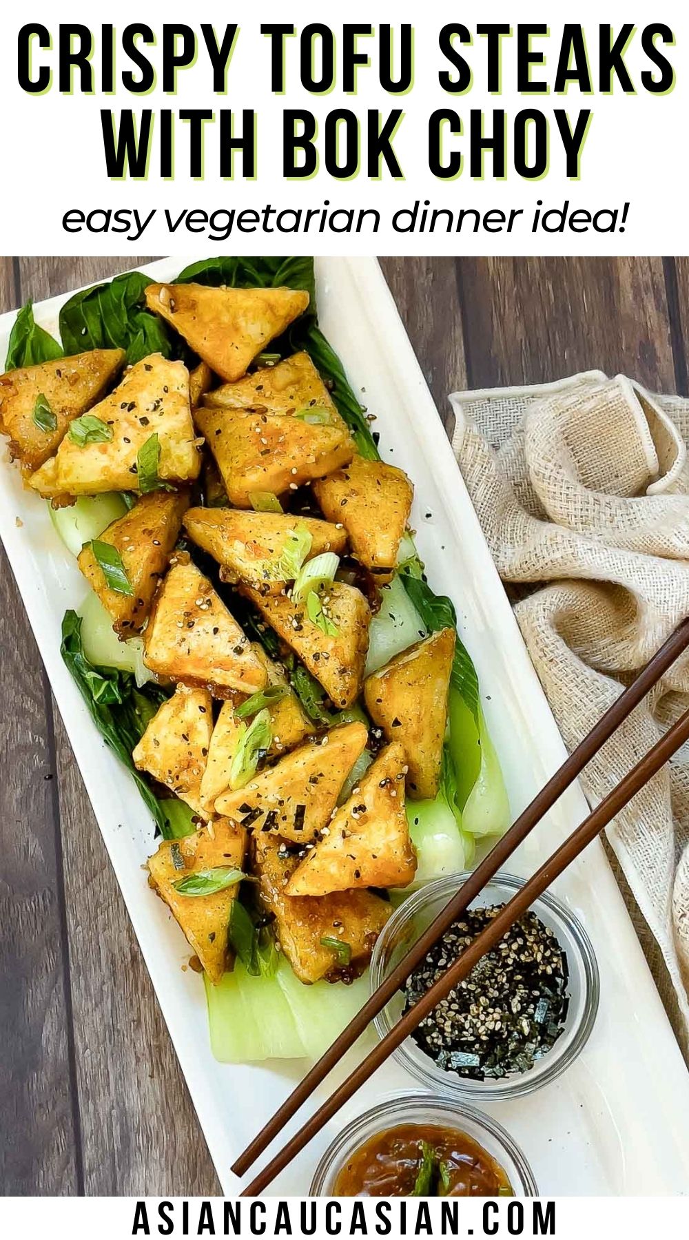 Golden-brown, crispy tofu steaks piled on top of cooked baby bok choy and sprinkled with seasonings plated on top of a white serving platter with small bowl of sauce and furikake seasoning on the side, and a pair of chopsticks on top and a napkin on the side.