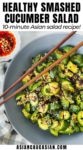 Smashed cucumber salad in a gray bowl with wooden chopsticks on top and a small white bowl of chili oil and a checkered napkin on the side.