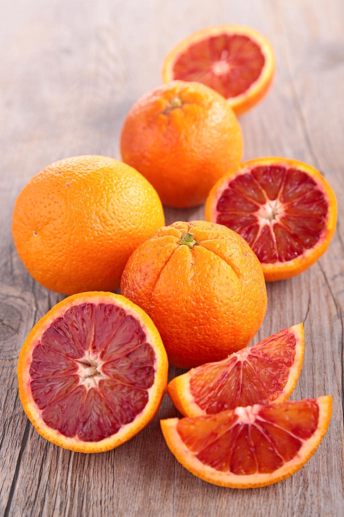 Whole and halved blood oranges on top of a wooden board