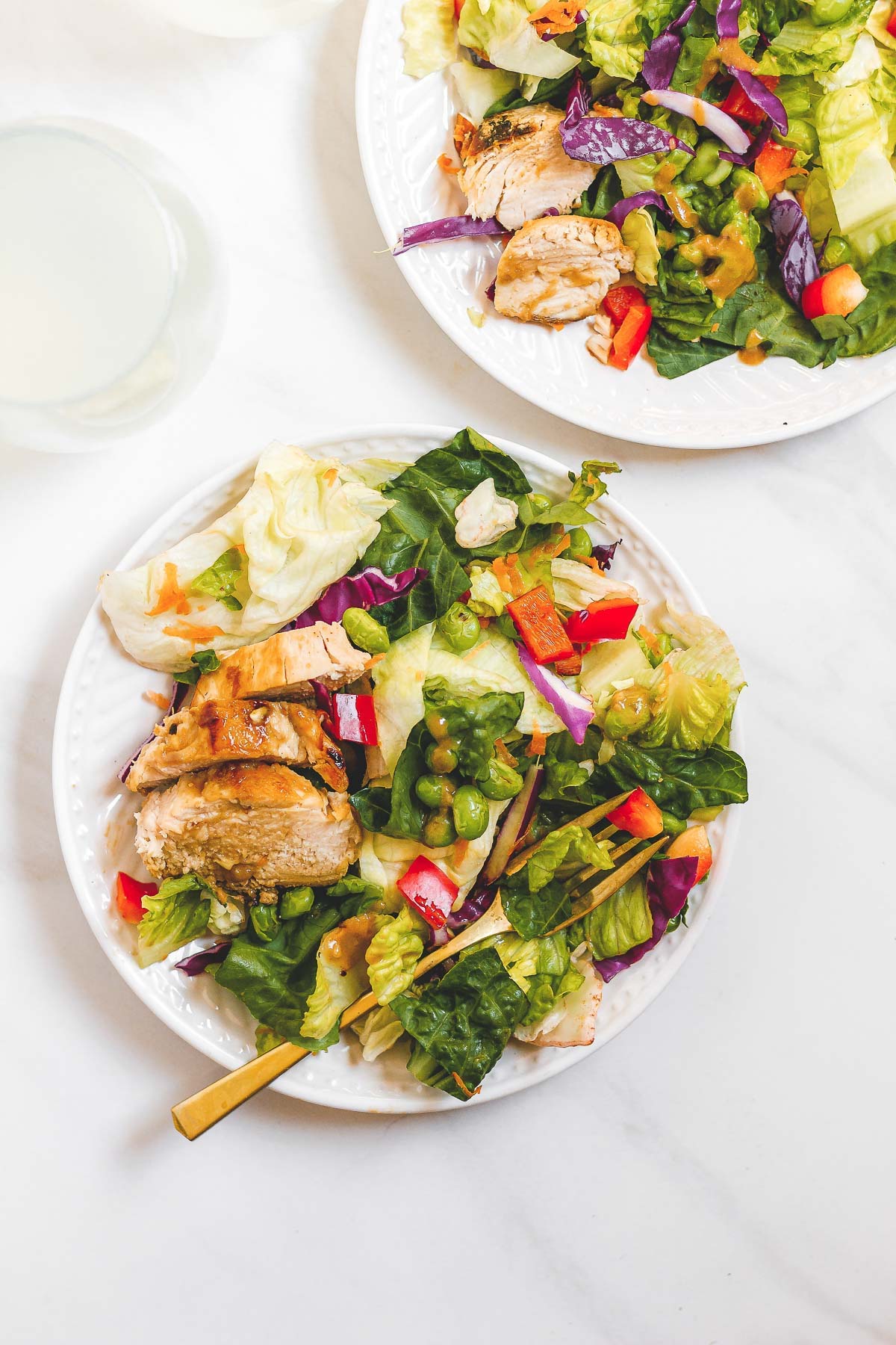Two white bowls with Spicy Thai Salad with Chicken with a fork on top placed on top of a marble surface.