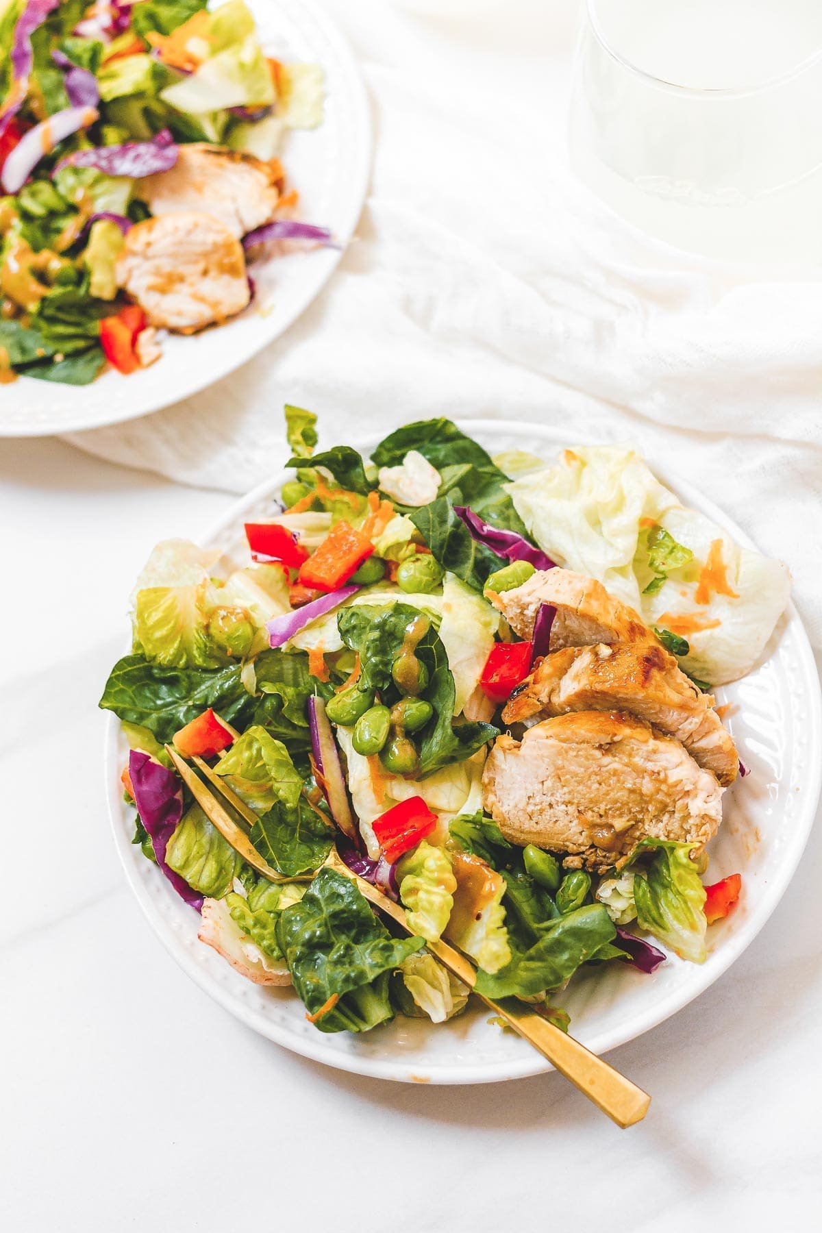 Two white bowls with Spicy Thai Salad with Chicken with a fork on top placed on top of a marble surface.