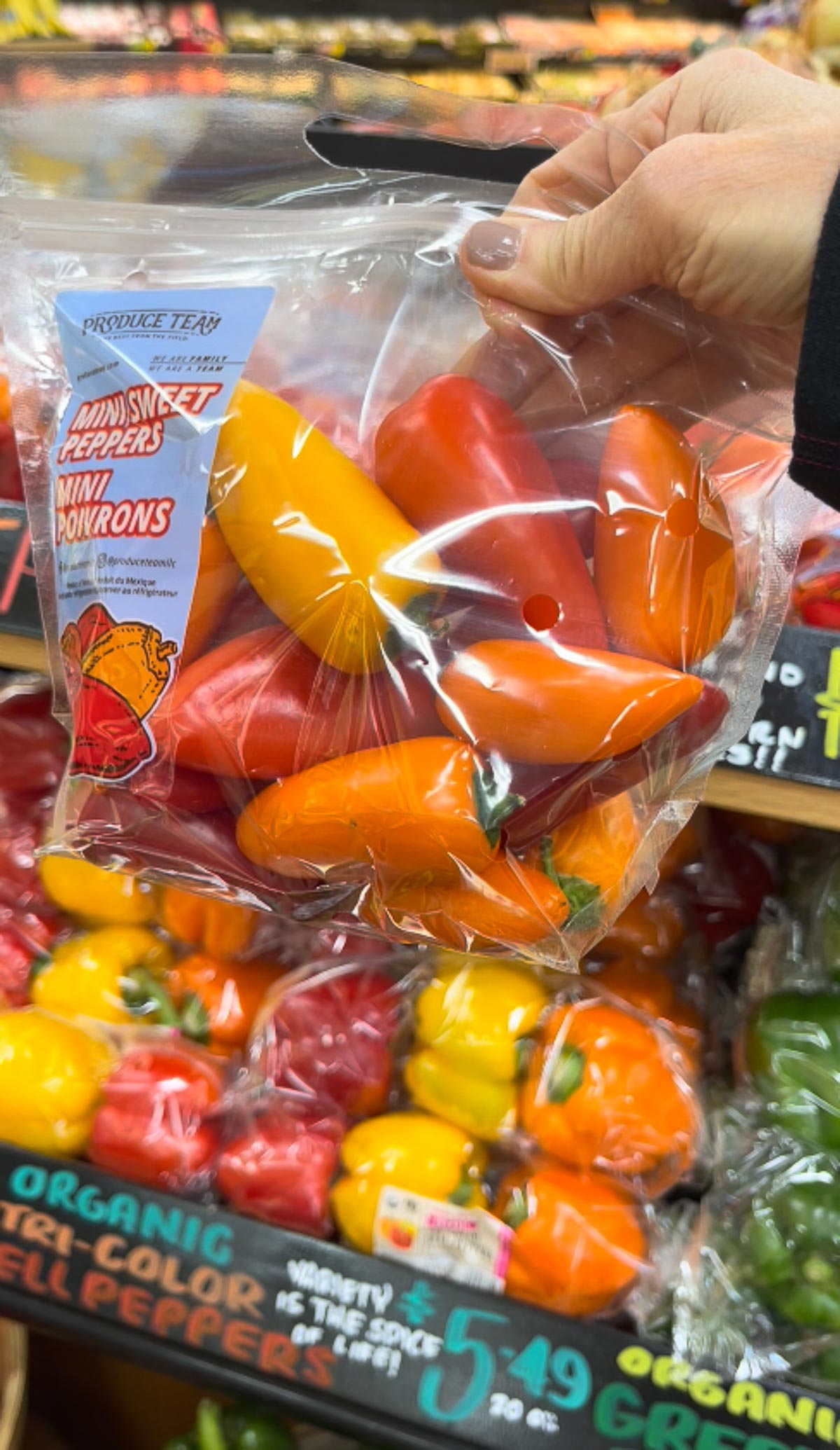 A hand holding up a bag of Trader Joe's colorful mini bell peppers.