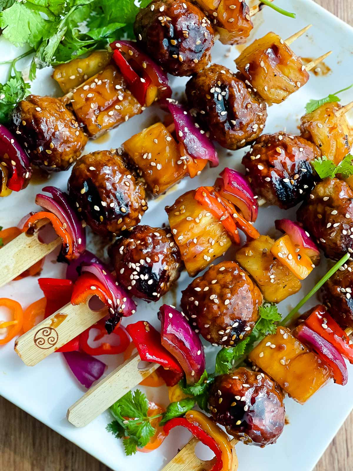 Grilled turkey meatball skewers placed on top of a white serving platter with green herbs on the side.