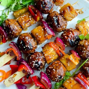 Grilled turkey meatball skewers placed on top of a white serving platter with green herbs on the side.