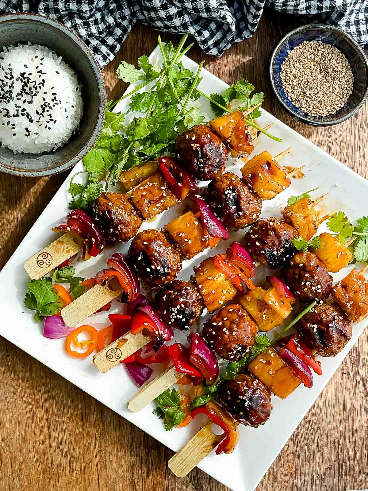 Grilled turkey meatball skewers placed on top of a white serving platter with white rice and sesame seeds on the side.