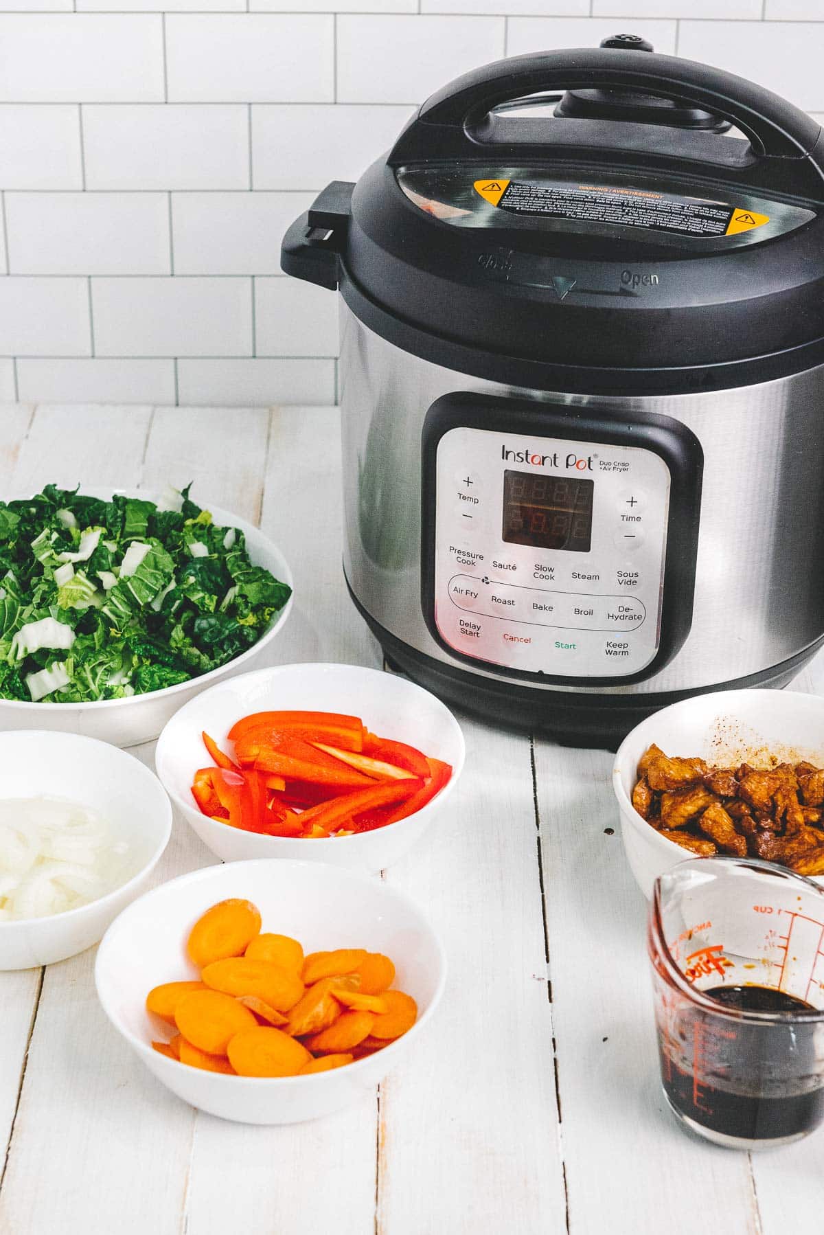 Ingredients in white bowls for Instant Pot Pork Lo Mein on a white board with an Instant Pot in the background