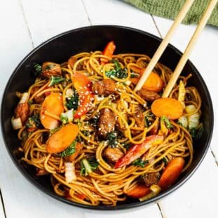 Pork Lo Mein in a black bowl with chopsticks and a green napkin on top of a white board.