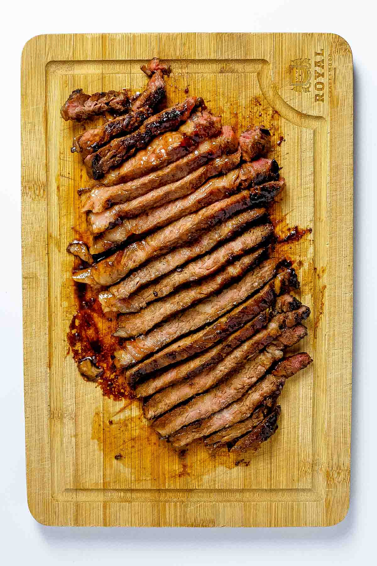 Sliced beef steak just off the grill resting on a wooden cutting board.