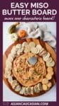 a miso butter board on a round wooden board surrounded by crackers and bread with baby pumpkins and a napkin on the side