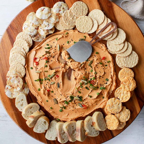 a miso butter board on a round wooden board surrounded by crackers and bread with baby pumpkins and a napkin on the side