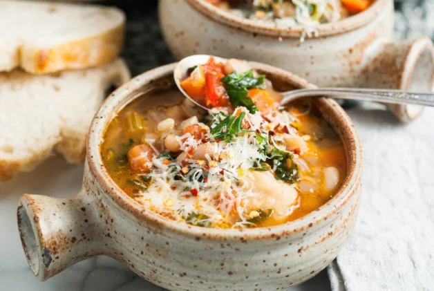 A bowl of chunky Ribollita Italian bean soup with a spoon inserted and other bowls behind it.