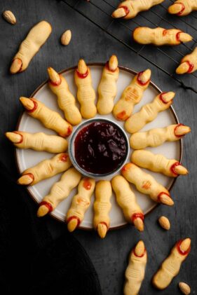 creepy witch finger cookies for Halloween on a round plate with finger nails made from almonds and a sweet dipping sauce in a small bowl in the middle
