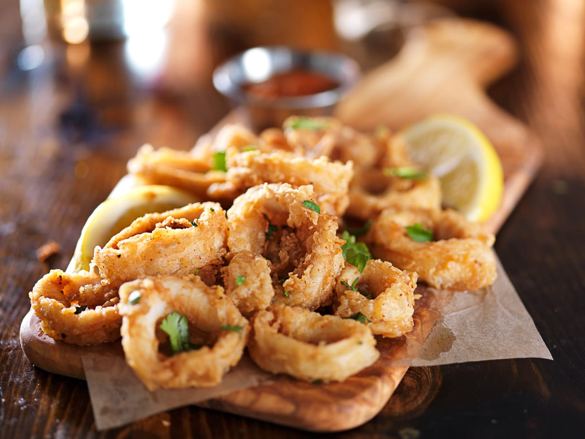 Fried and crispy calamari rings on a wooden board with lemon wedges on the side.