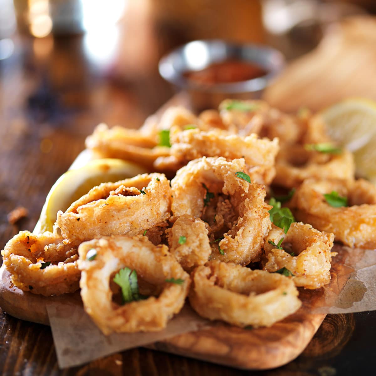 Fried and crispy calamari rings on a wooden board with lemon wedges on the side.