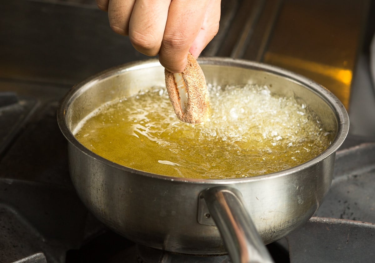 Calamari ring being placed into a pan of hot bubbling oil.