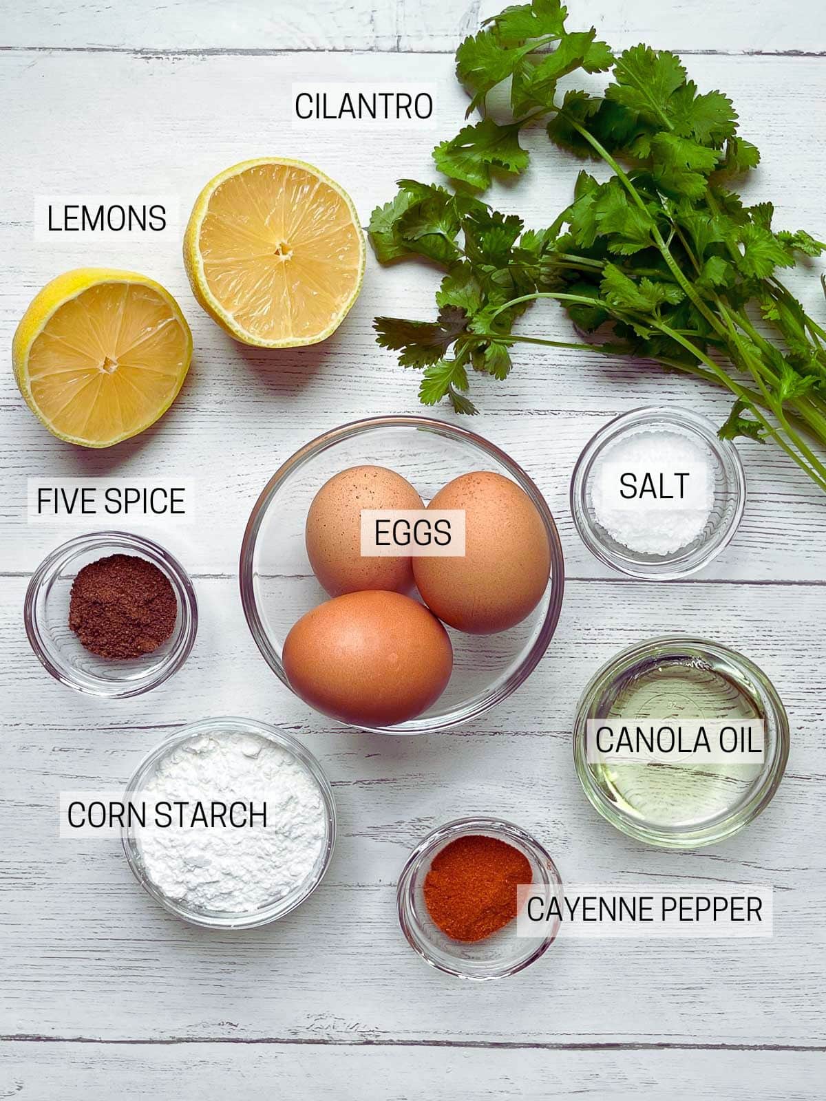 Labeled ingredients for making crispy fried calamari on top of a white board with fresh herbs on the side.