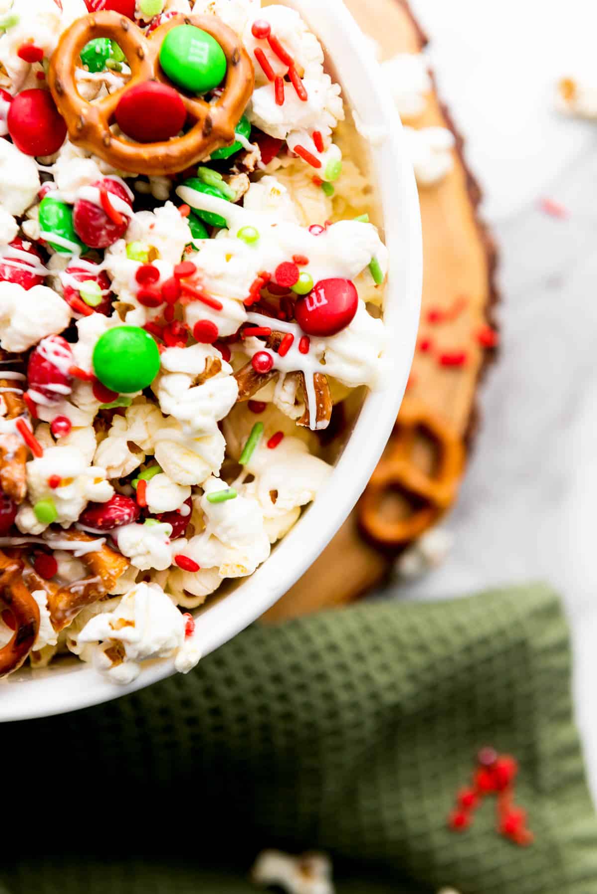Close up of festive Christmas popcorn Santa munch in a white bowl on top of a wooden board with a green napkin on the side.