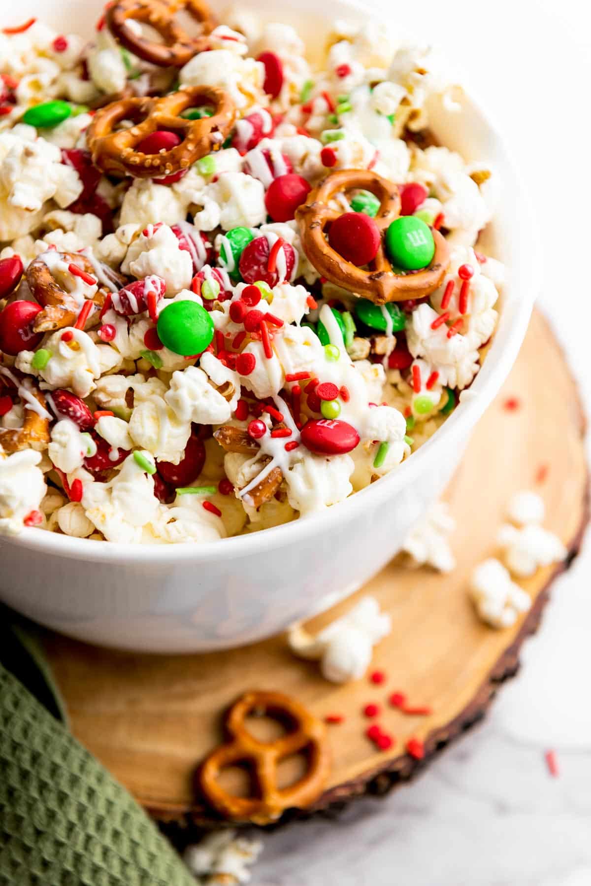 Christmas popcorn Santa munch in a white bowl on top of a round wooden board with a green napkin on the side.