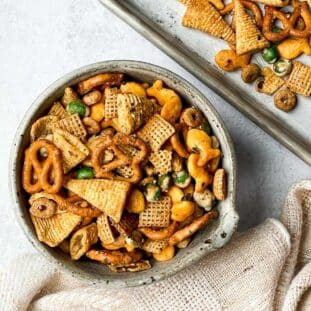A bowl of Furikake chex mix with a linen napkin on the side and a baking tray in the background.