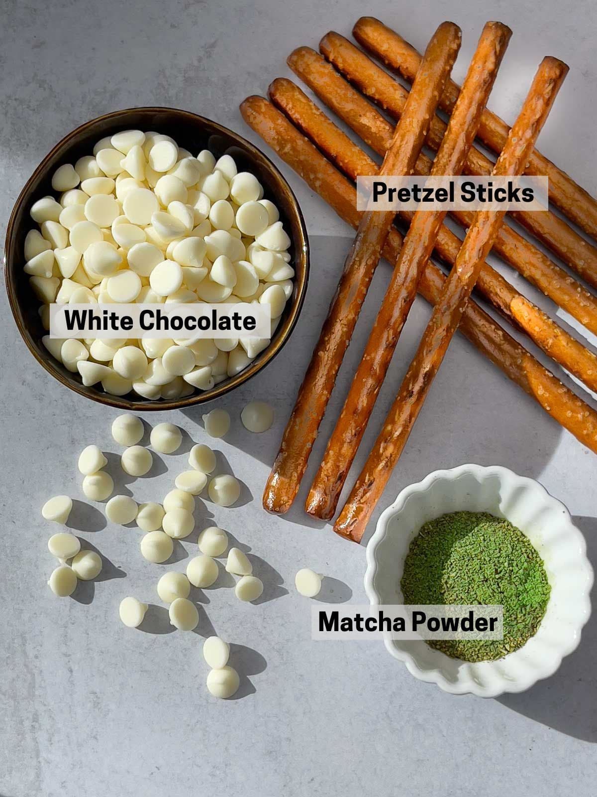 Labeled ingredients for making Matcha Chocolate Dipped Pretzels on top of a gray surface.