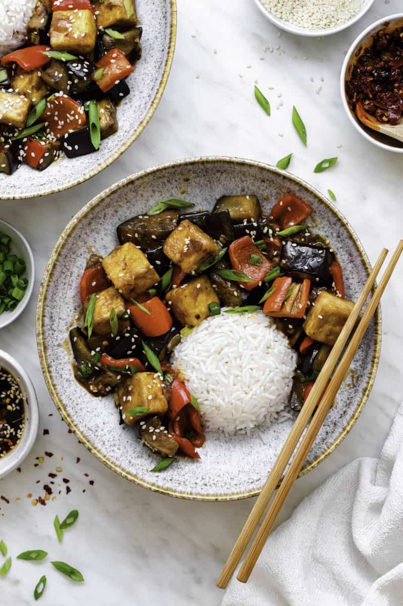 Panda express eggplant tofu in two white bowls with white rice and chopsticks and sauces on the side.