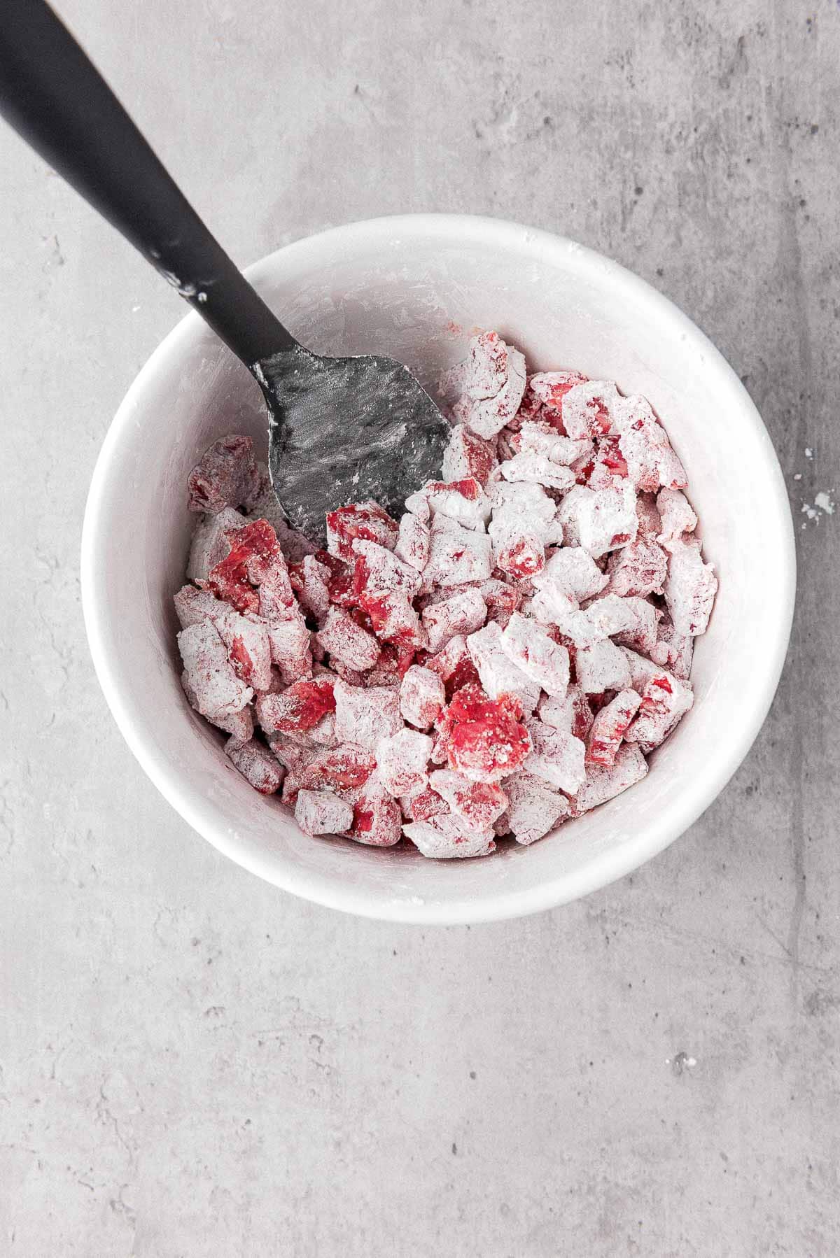Flank steak cubes coated with corn starch in a white bowl with a black spoon.