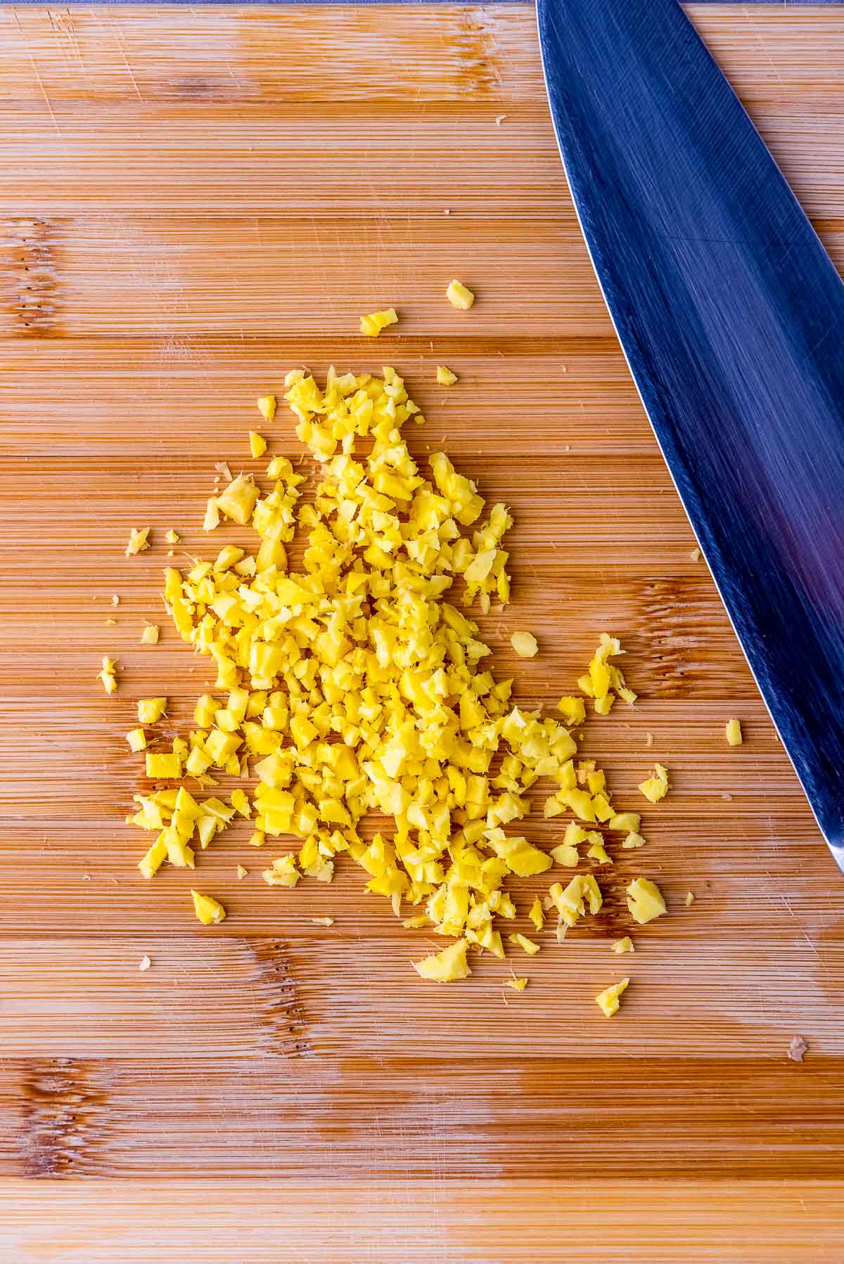 Minced ginger on a wooden cutting board with a large knife on the side.