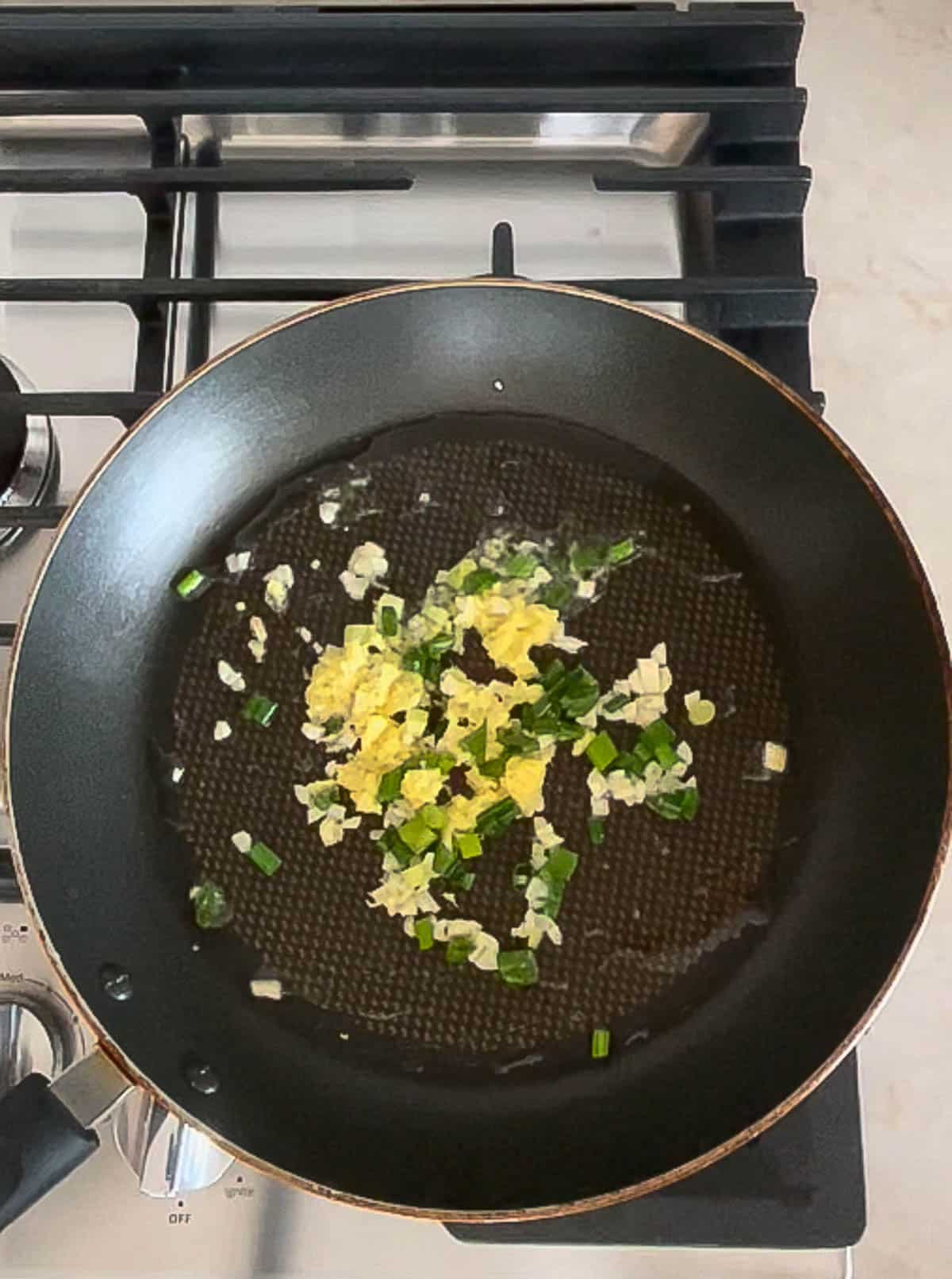Sauteed ginger, garlic, and scallions in a frying pan on to of a stove.