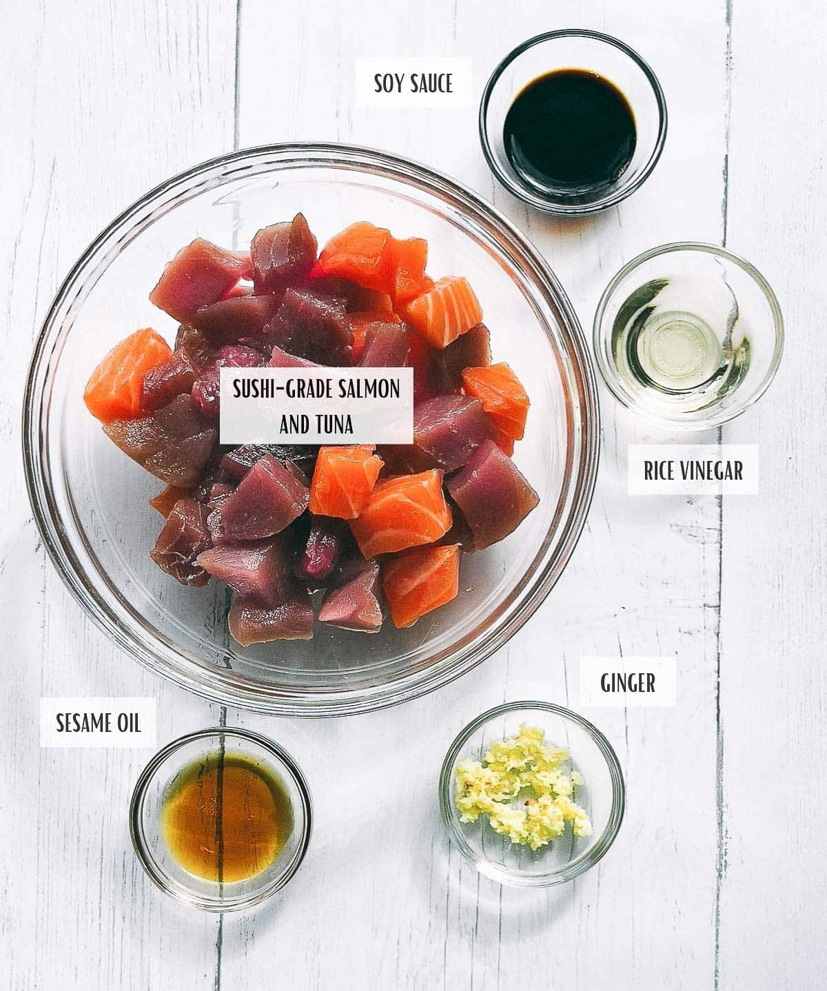 Labeled ingredients in glass bowls for making Sushi Waffles with Salmon and Tuna on top of a white surface.