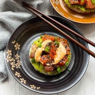 Sushi waffles with salmon and tuna on two round plates with a side of chopsticks on top of a white surface with a napkin on the side.