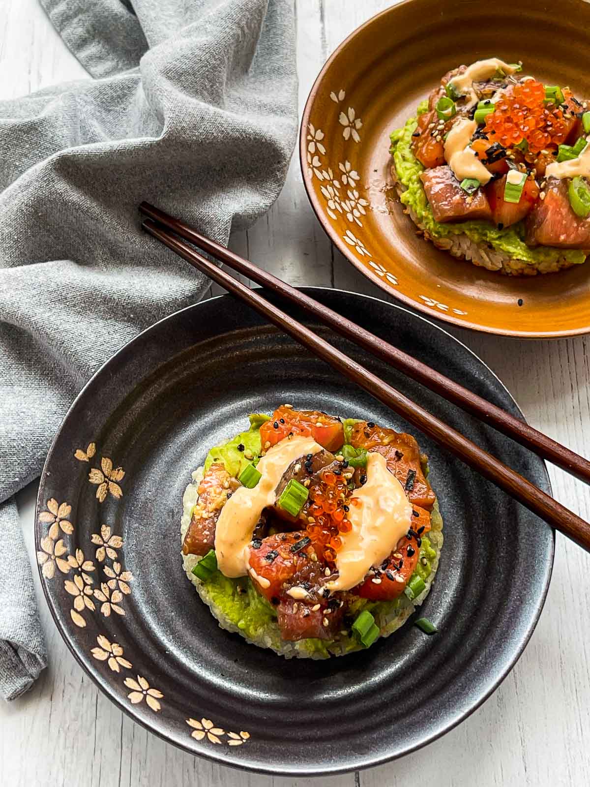 Sushi waffles with salmon and tuna on two round plates with a side of chopsticks on top of a white surface with a napkin on the side.