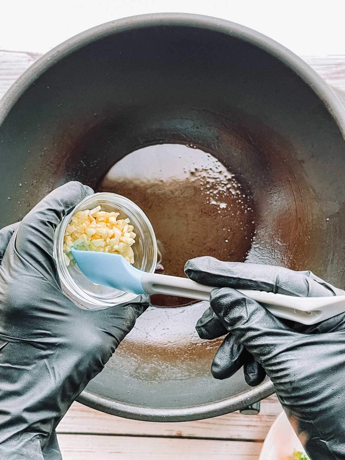 Hands adding minced garlic in a small glass bowl to a hot wok.