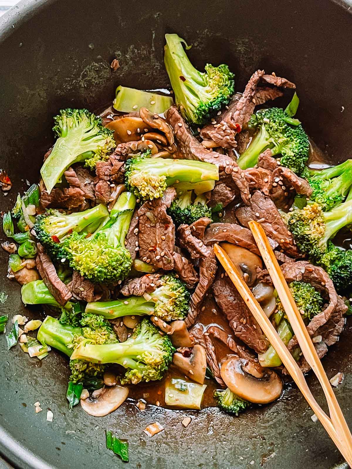 Beef and broccoli stir fry in a large wok with a pair of wooden tongs.