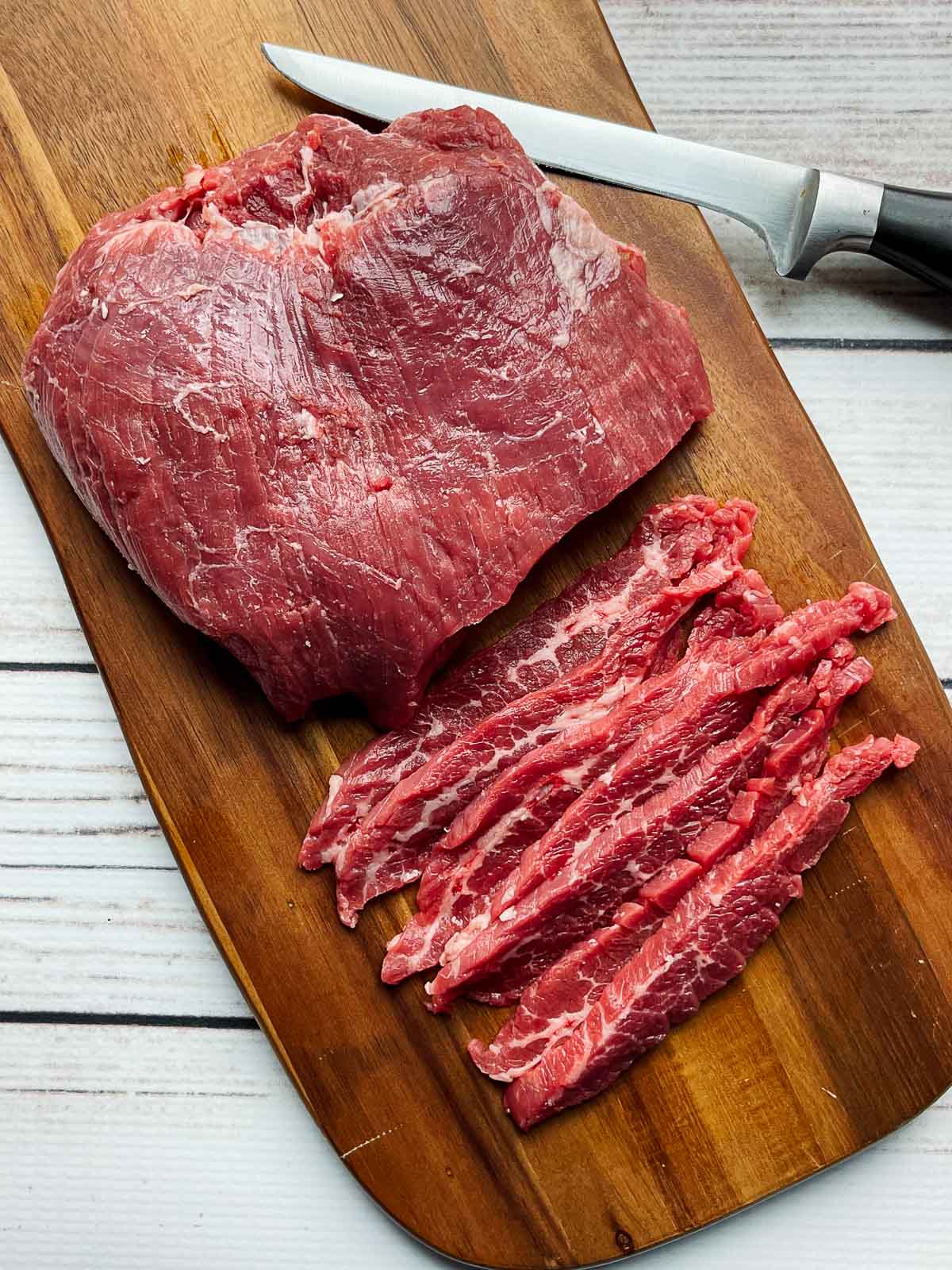 Flank steak on a wooden board with slices and a filet knife on the side.