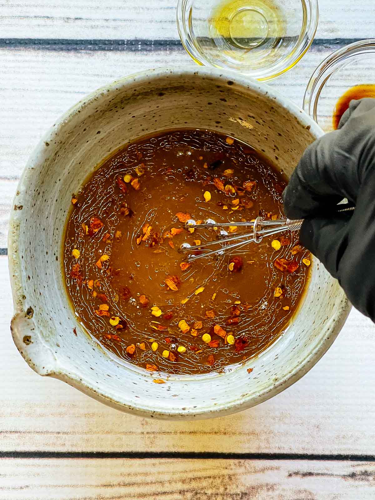 Whisking the sauce for beef and broccoli stir fry in a small mixing bowl with empty glass bowls on the side.