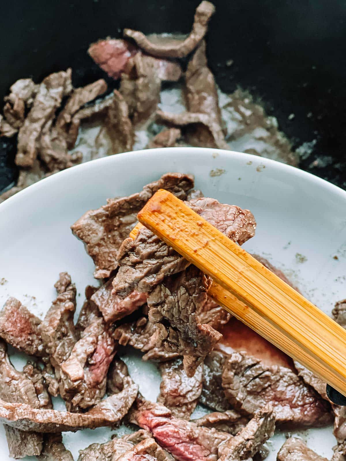 Seared flank steak strips being added to a wok.