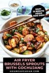 Air fryer brussels sprouts with gochujang in a white bowl topped with chopsticks with a blue napkin and garnishings in small bowls on the side on top of a white board.