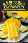 Mango coconut lime popsicles on a white plate with slices of lime on top and more popsicles in the background with a whole mango.