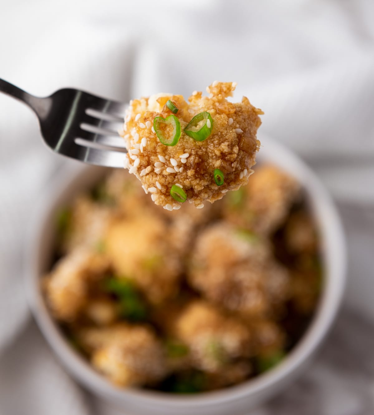 A fork lifting a teriyaki cauliflower wing over a bowl of cauliflower wings.