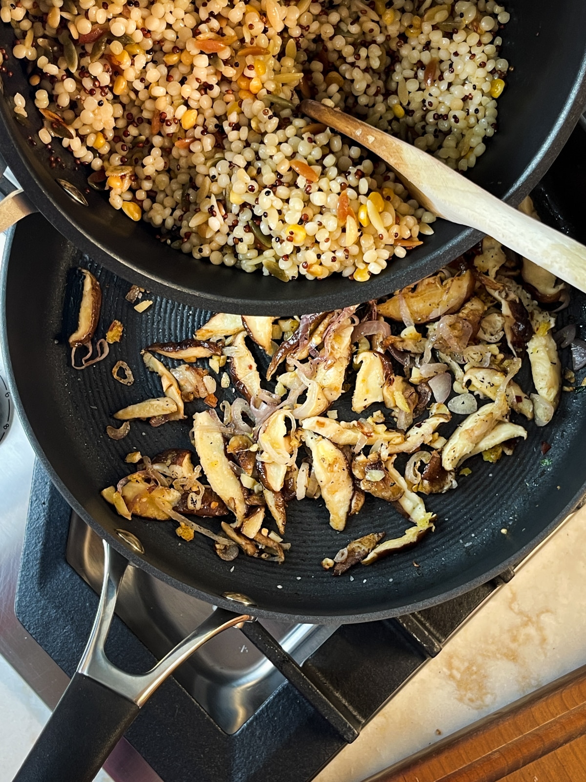 Cooked couscous and quinoa blend being poured into a frying pan with cooked shiitake mushrooms and shallots.