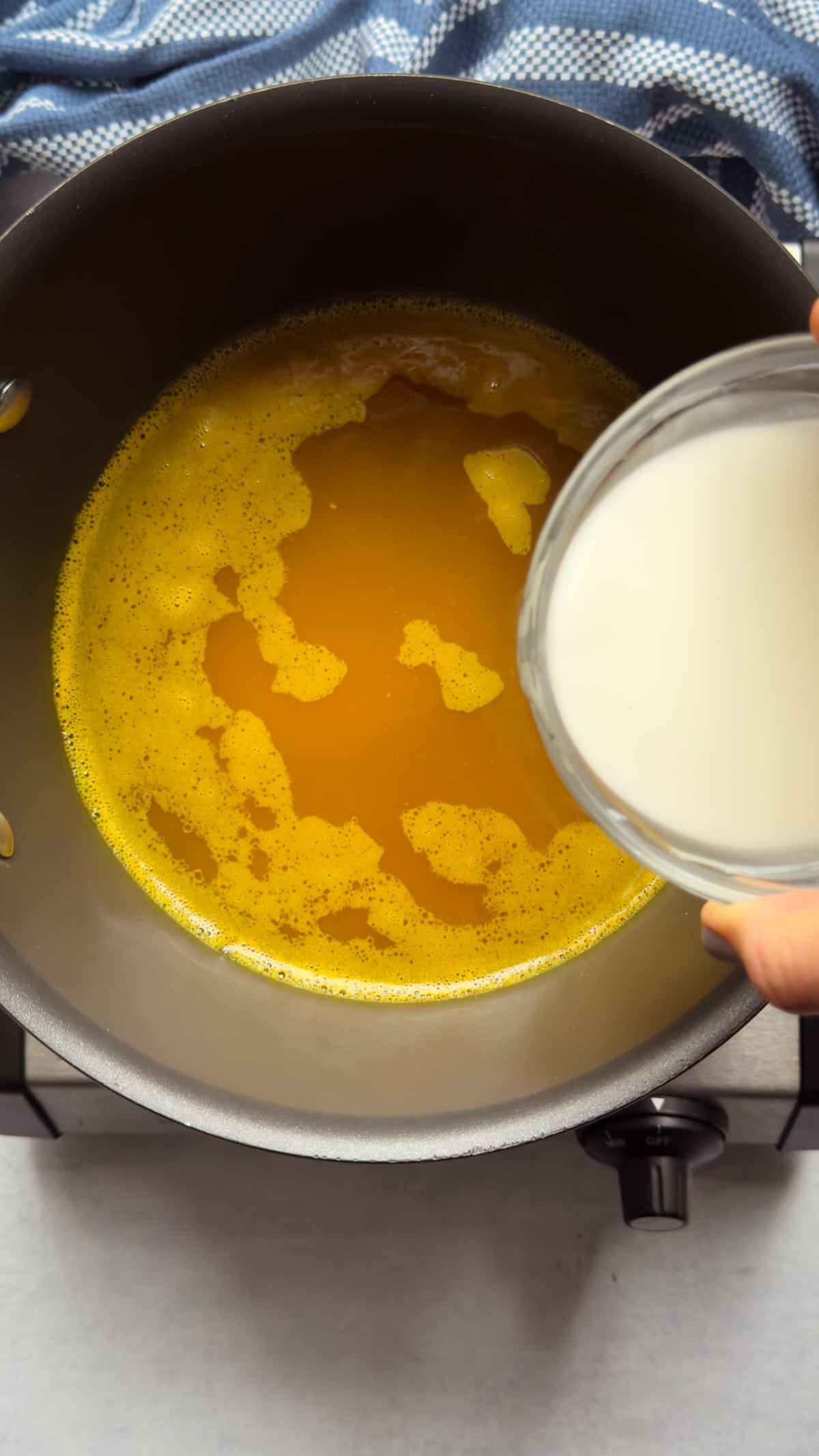 A cornstarch slurry in a glass bowl being added to Chinese egg drop soup broth in a pot with a blue napkin on the side.