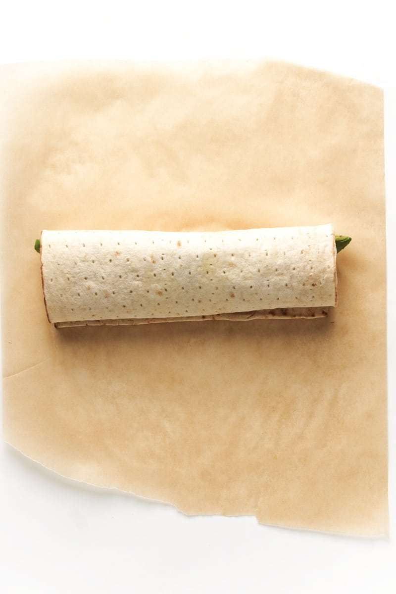 Wrapping a grilled tofu and zucchini wrap on top of parchment paper.