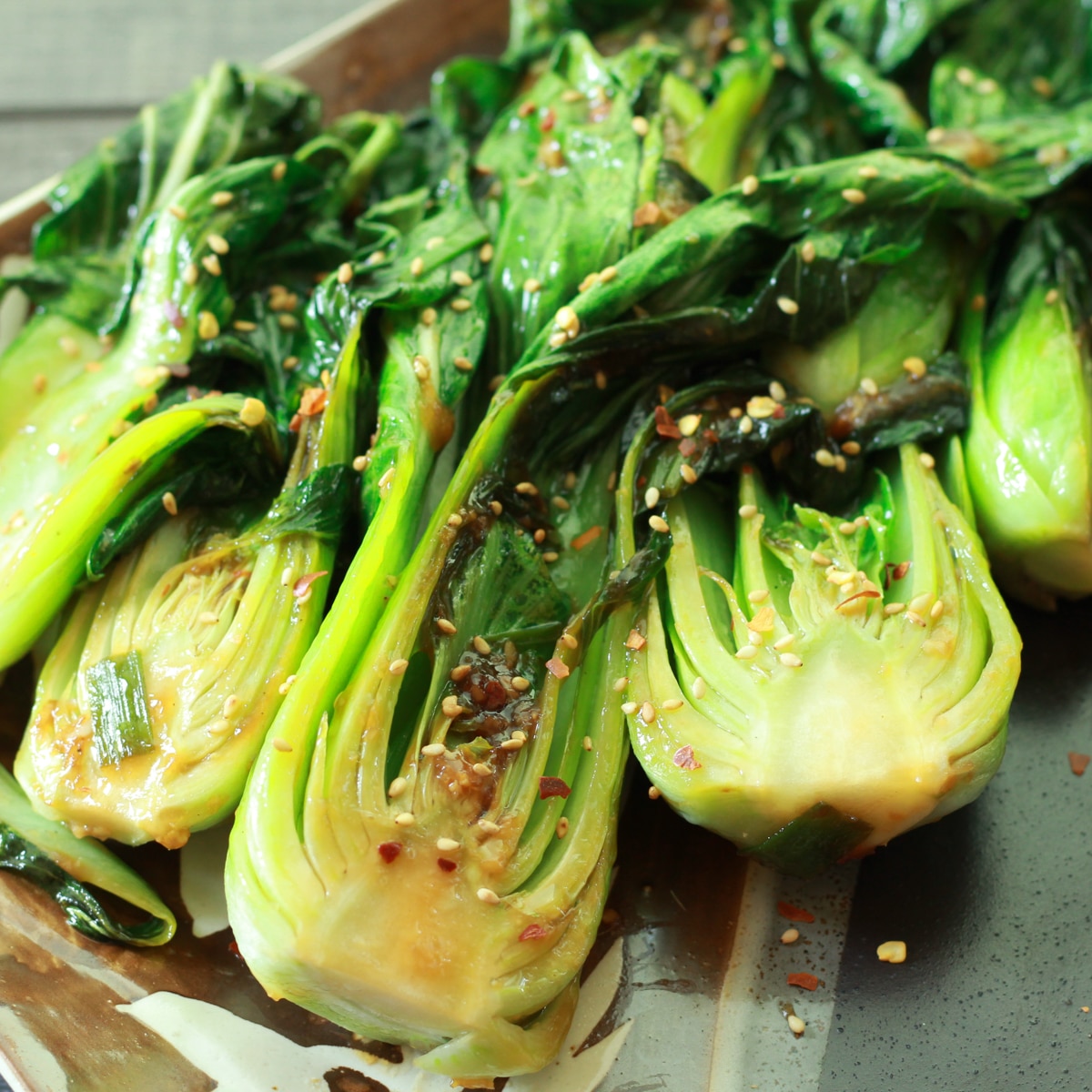 Cooked whole baby bok choy on a plate sprinkled with red pepper flakes.