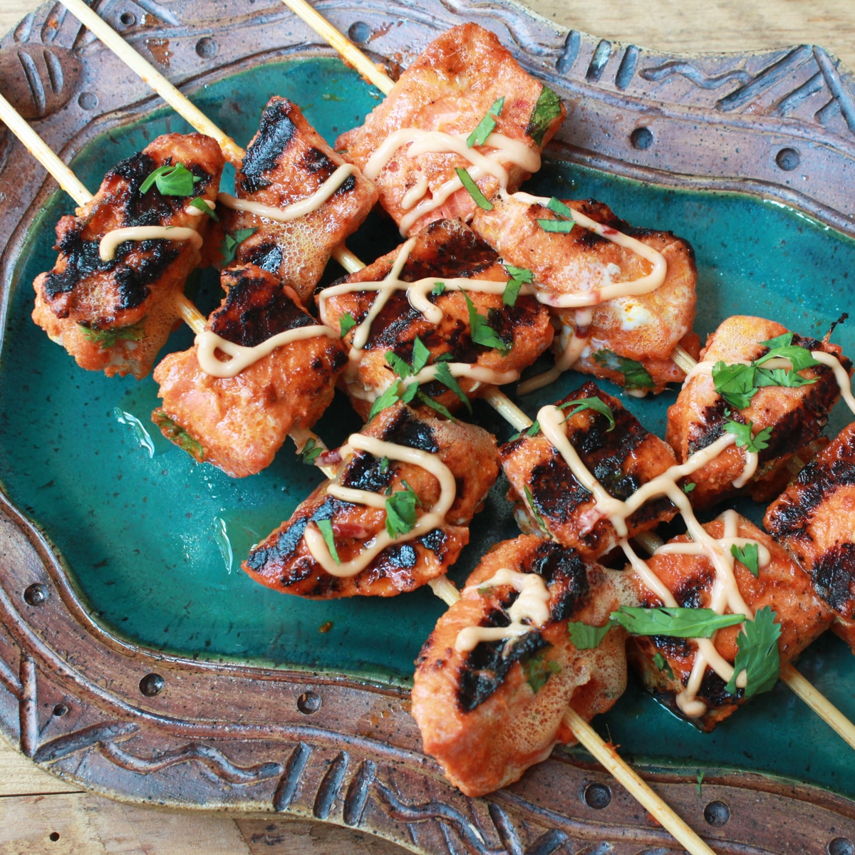 A healthy salmon recipe featuring grilled and cubed red curry salmon on three skewers drizzled with aioli on top of a green platter.