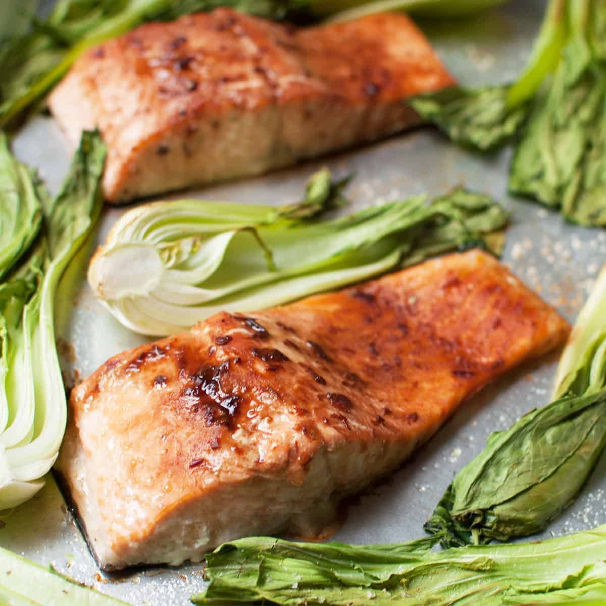 A healthy salmon recipe featuring filets of baked salmon and bok choy sprinkled with salt on top of a silver sheet pan.