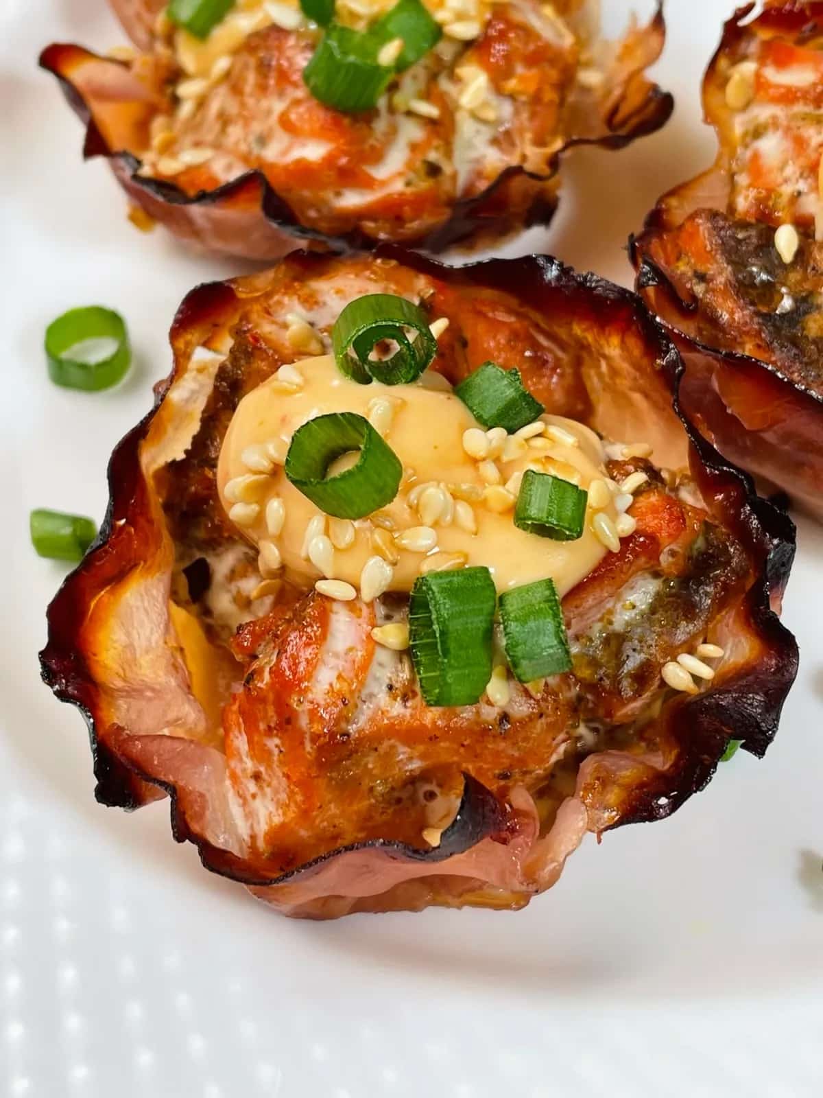Spicy baked salmon cups topped with slices of green onions on top of a white surface.