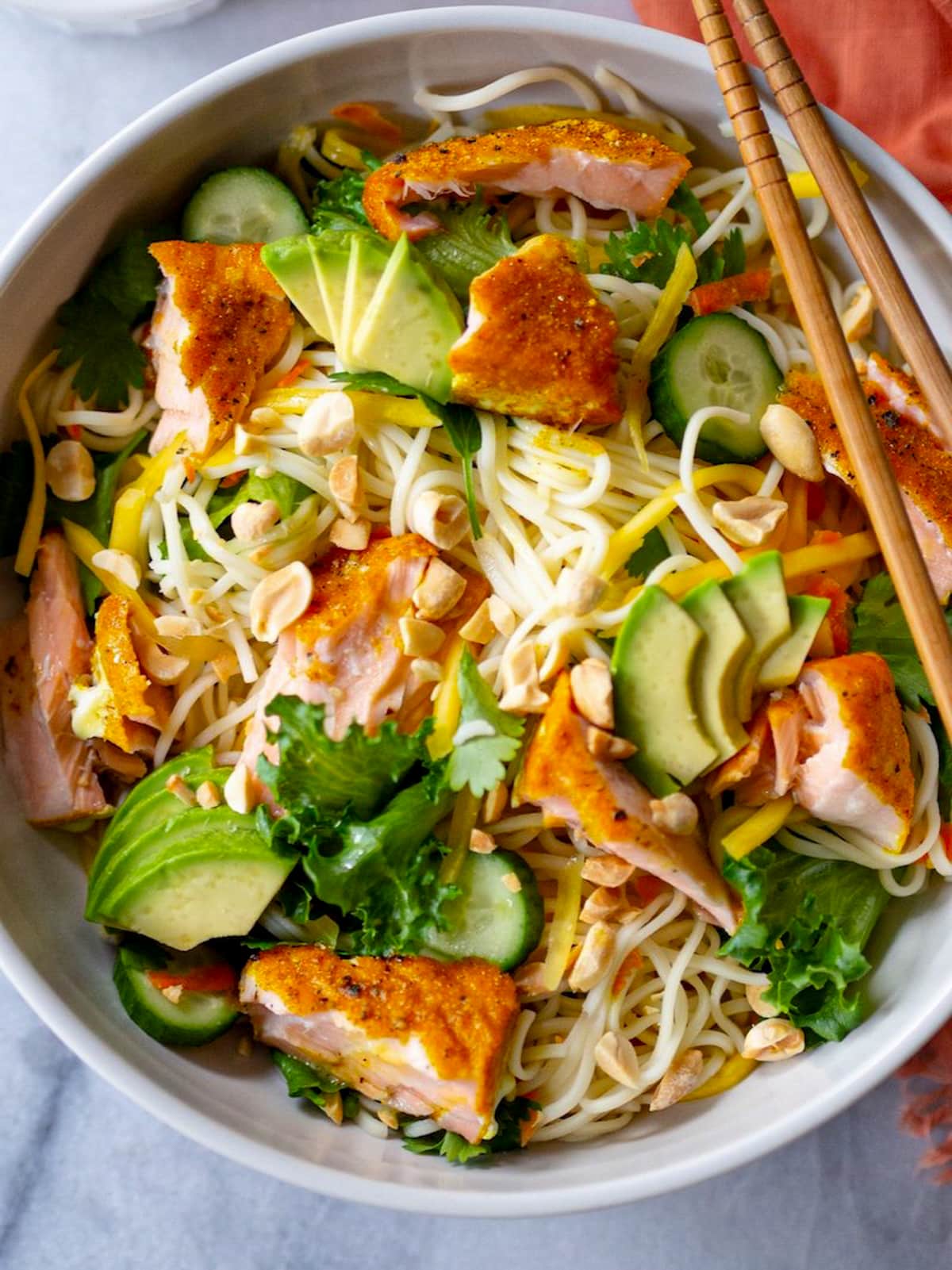 A large white bowl filled with Vietnamese curry salmon noodle salad with a pair of chopsticks on the side.
